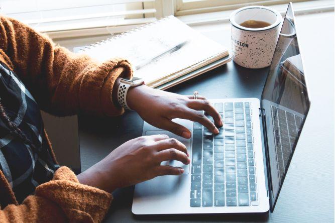 Person typing on a laptop with a cup of coffee  on the side